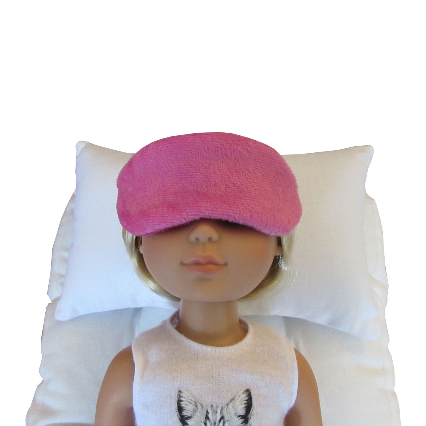 A bright pink panne velvet sleep mask worn by a doll lying on a white pillow, against a plain white background.