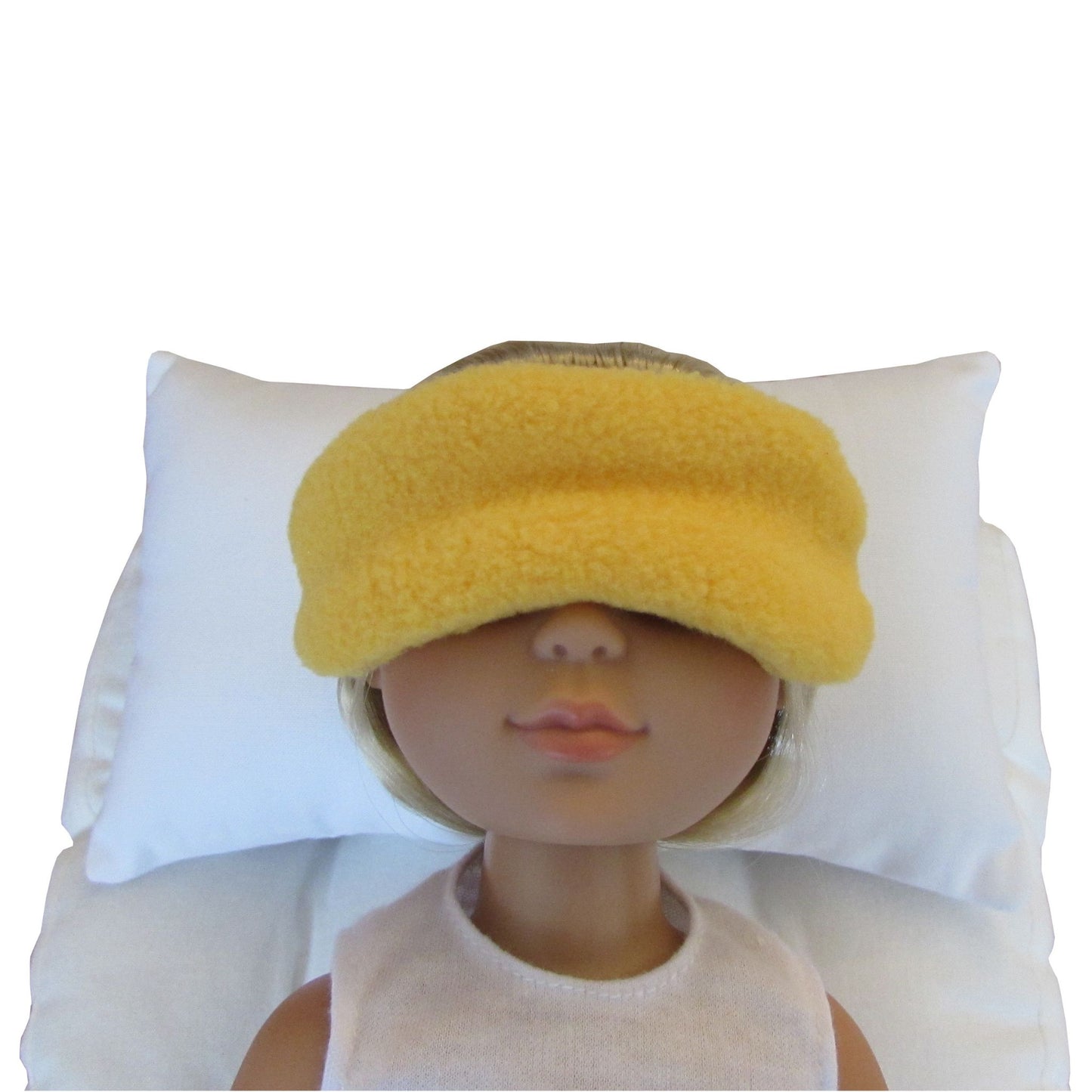A yellow fuzzy sleep mask worn by a doll lying on a white pillow against a white background.