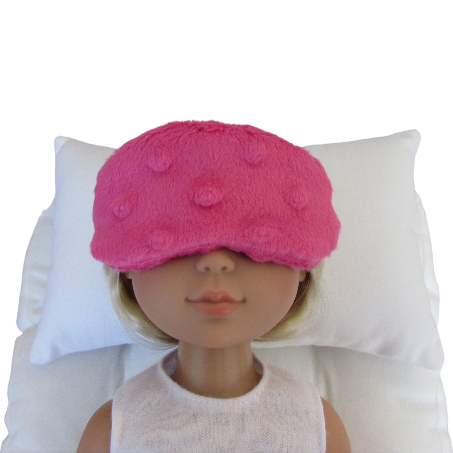 A hot pink minky sleep mask with raised textured bumps, shown on a doll's head resting against a white pillow.