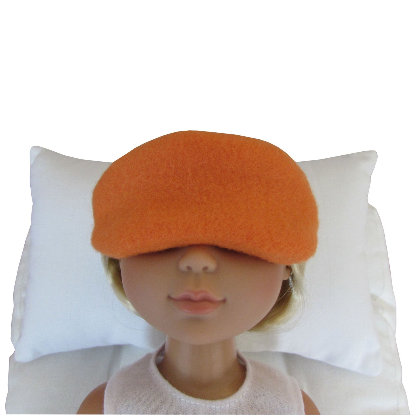 An orange fleece sleep mask shown on a doll's head, resting against a white pillow on a white background.
