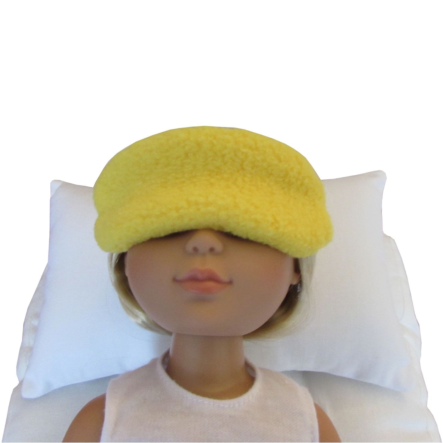 A yellow fuzzy sleep mask worn by a doll lying on a white pillow against a white background.