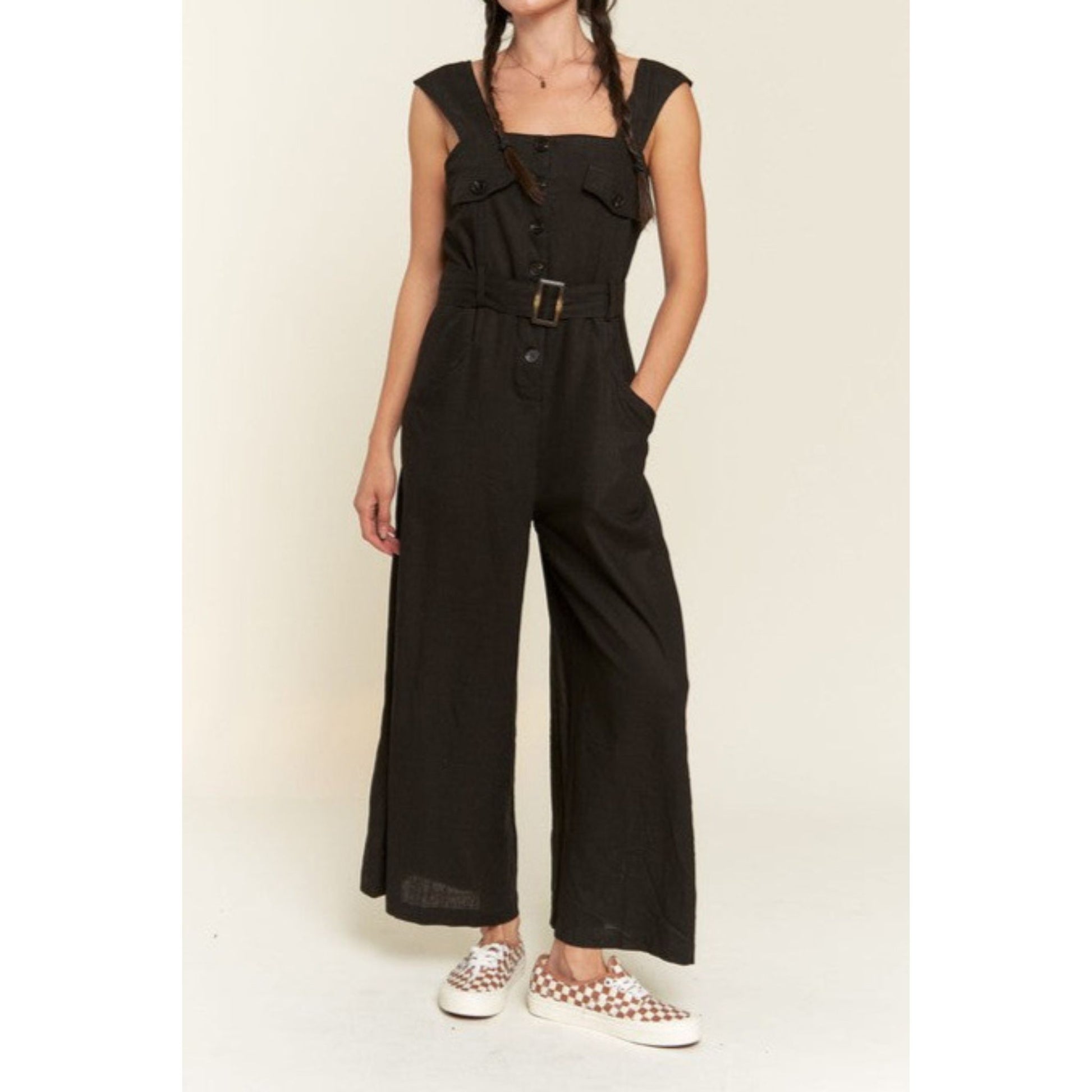 Person wearing a black jumpsuit with wide-leg pants on a beige background