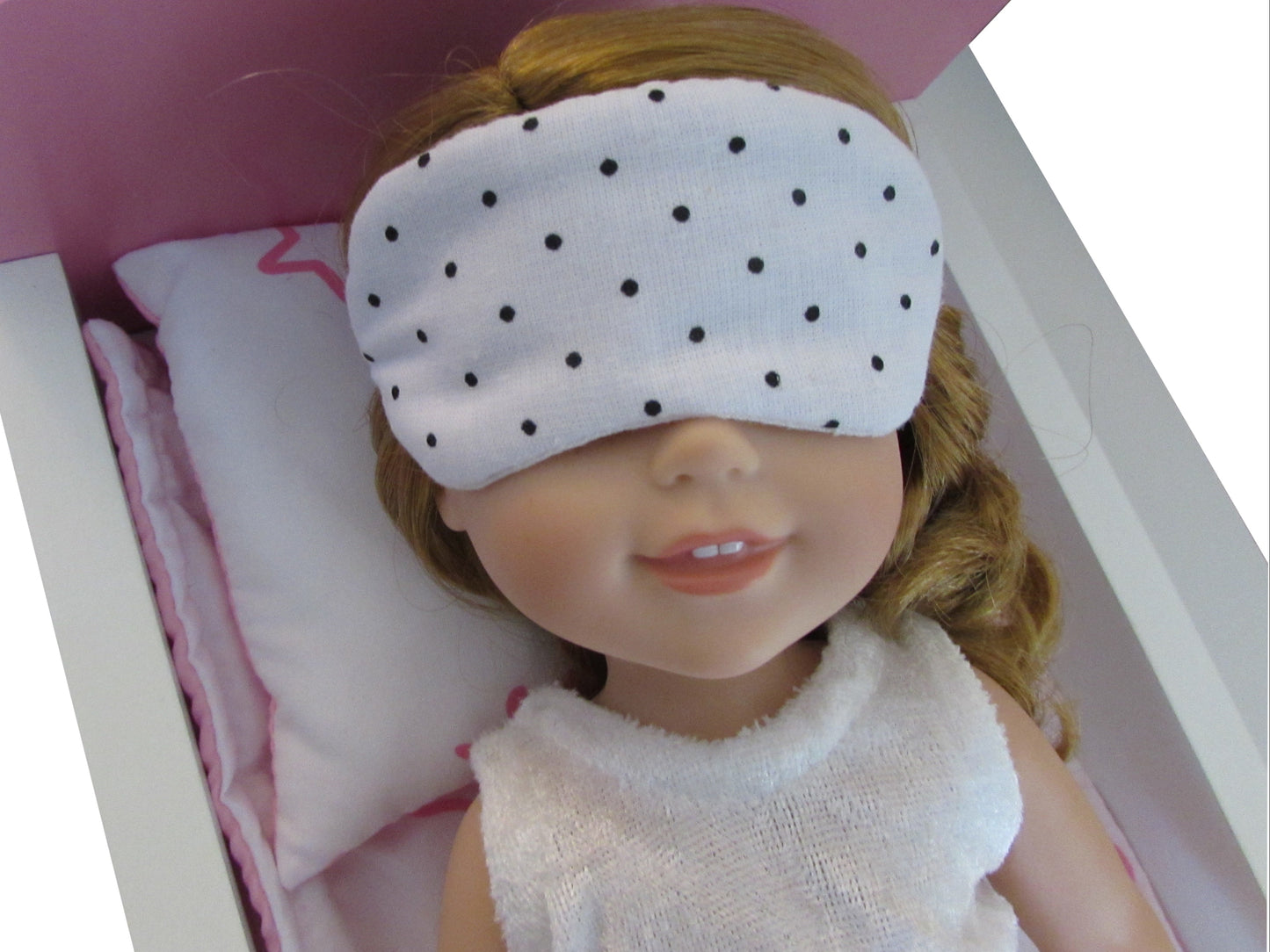 Doll with a polka dot eye mask on a pink bed