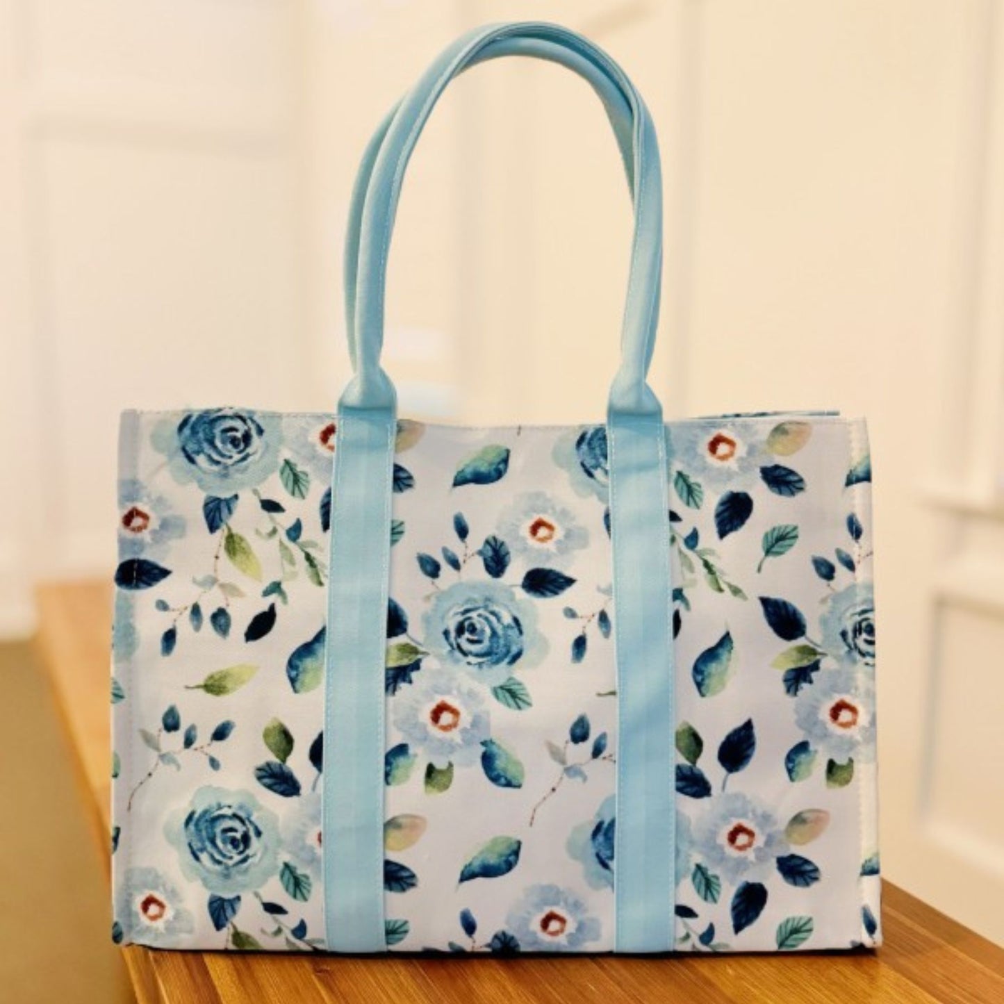 Floral-patterned tote bag with blue handles on a wooden surface.