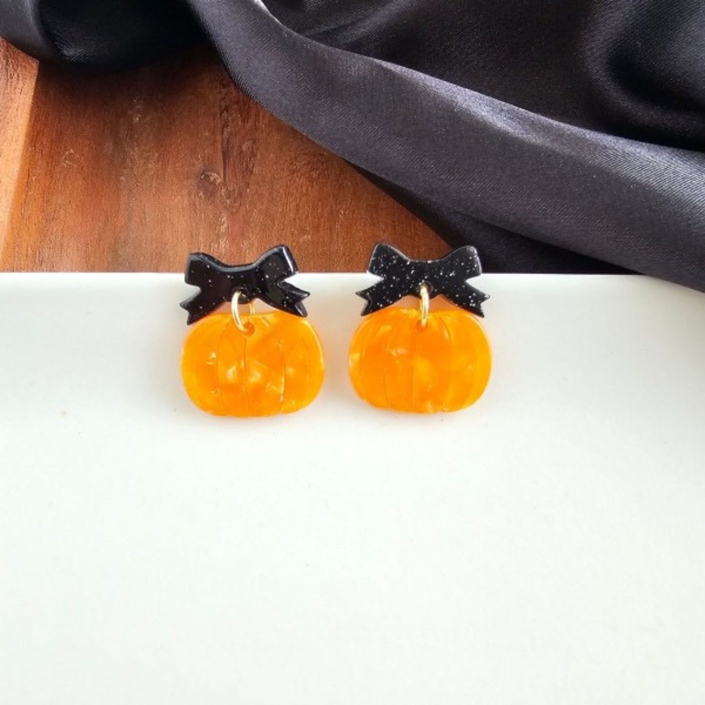 Pumpkin-shaped earrings with black bows on a white surface.