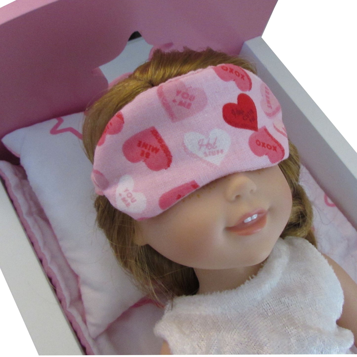 Doll wearing a pink sleep mask with heart patterns on a white background