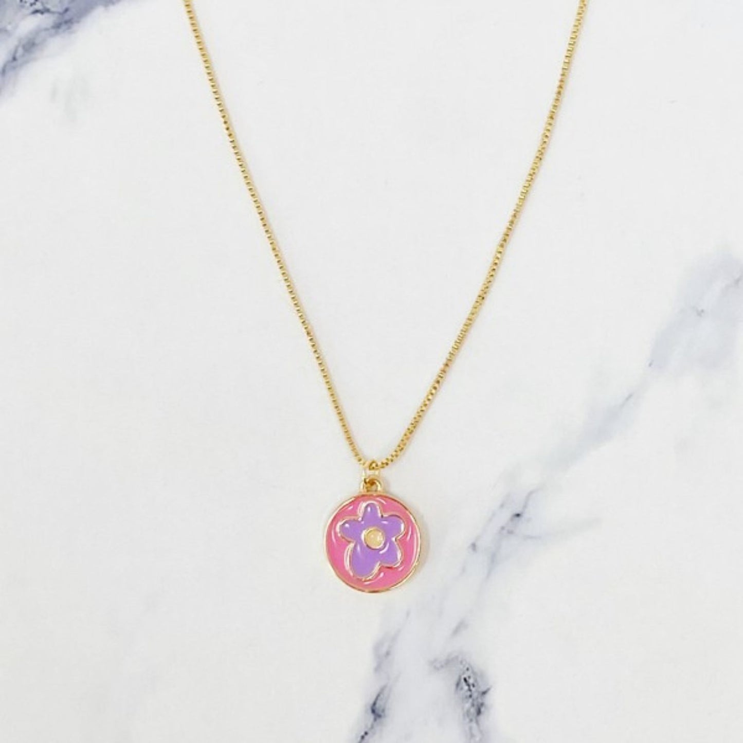 Gold necklace with a colorful flower pendant on a marble background