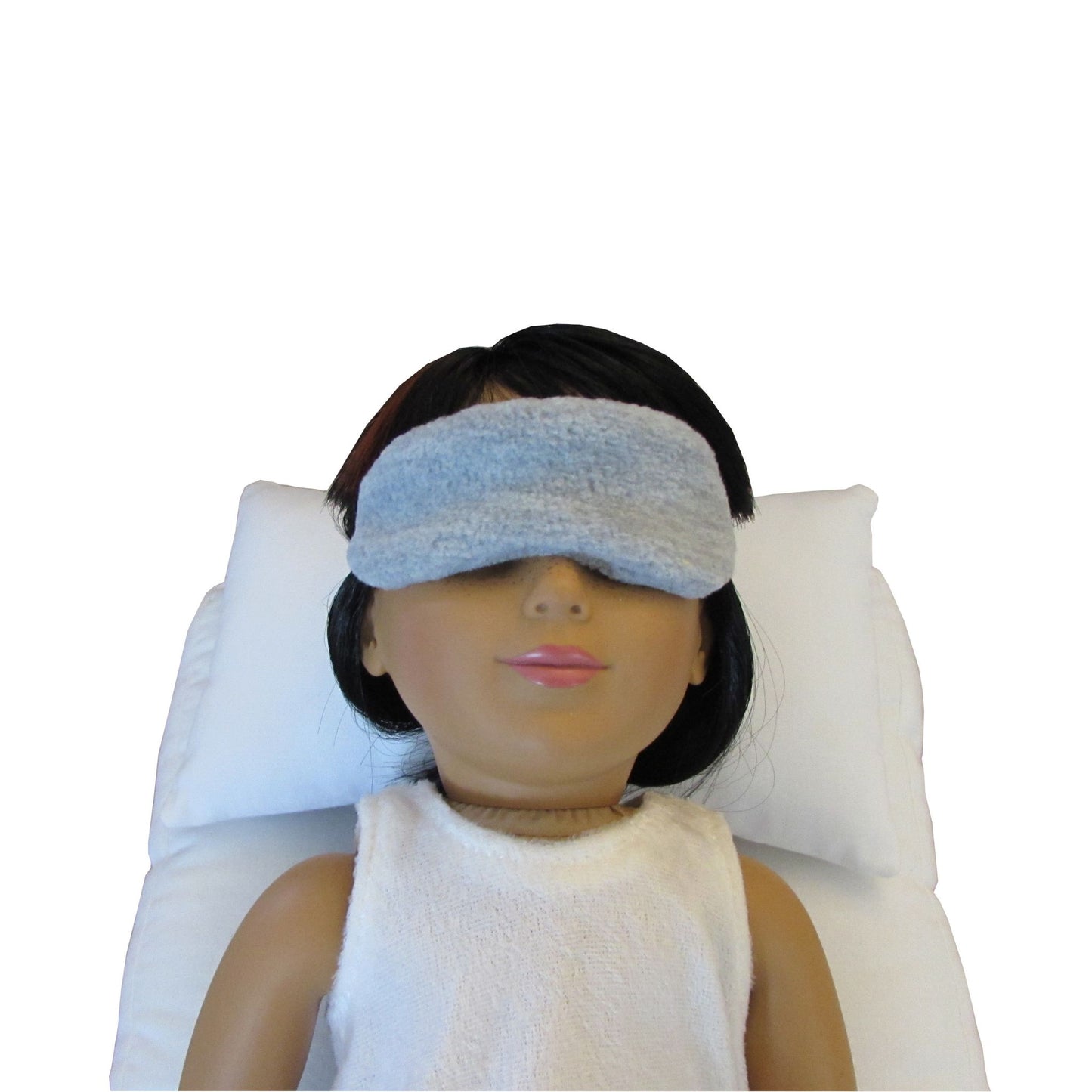 An 18-inch doll is wearing a gray anti-pill sleep mask while lying on a white doll pillow and a white doll mattress.