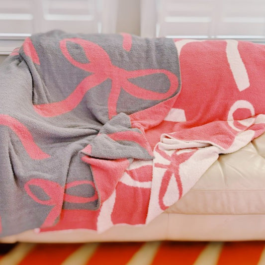 Gray and pink blanket with bow pattern draped over a bed.