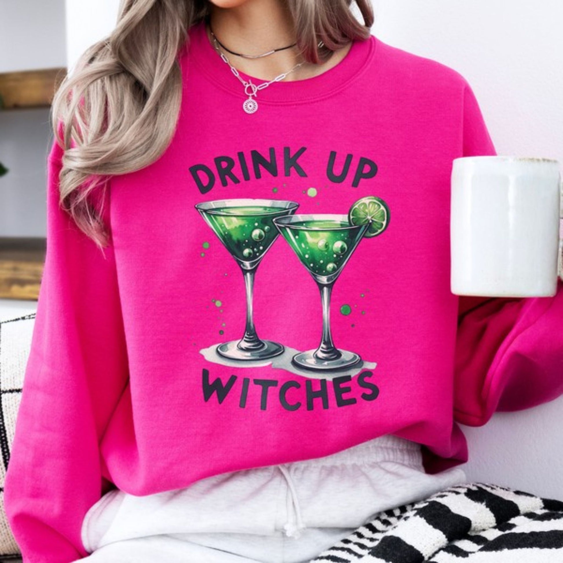 Person wearing a pink sweatshirt with 'Drink Up Witches' text and green cocktail graphics.