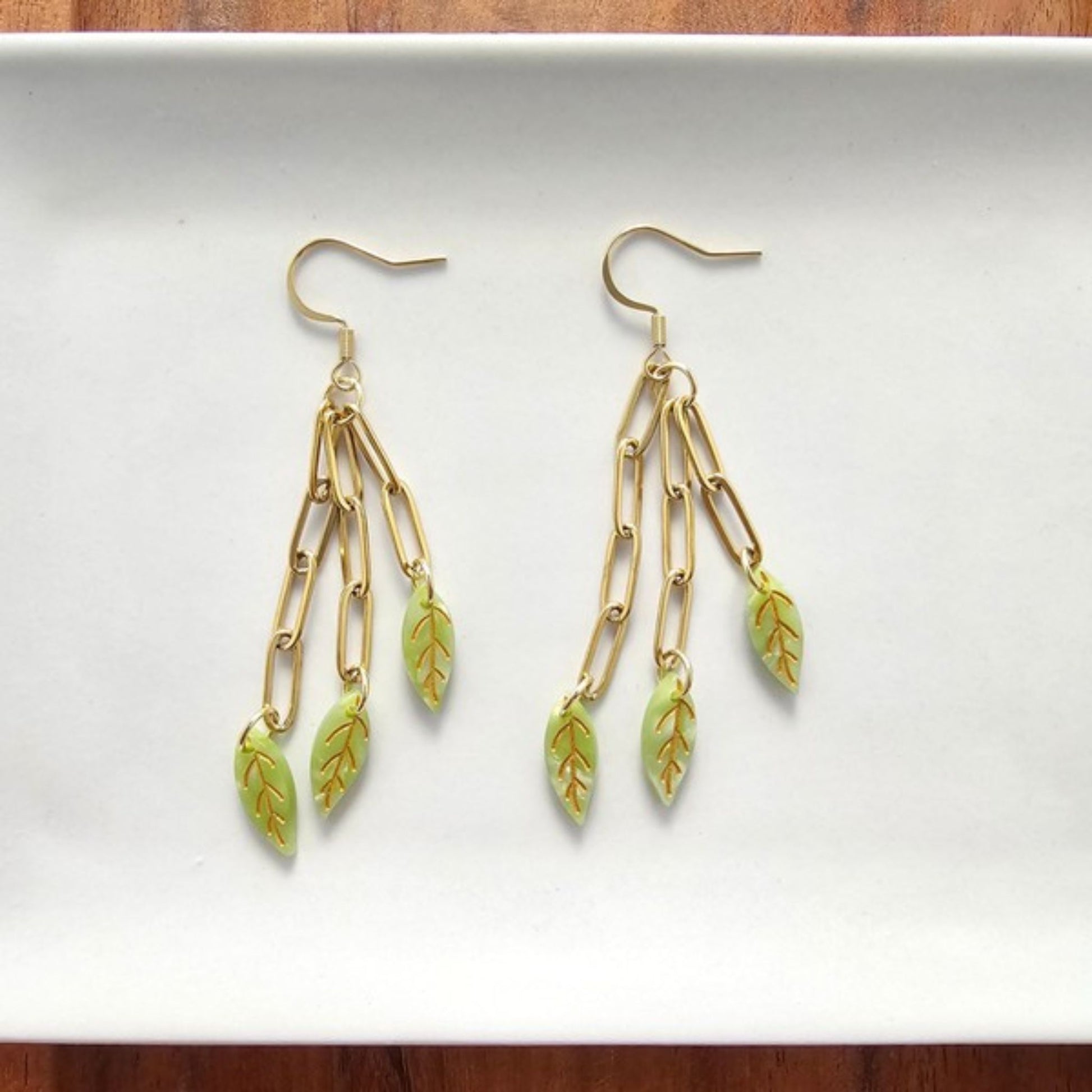 Gold and green leaf-shaped earrings on a white background