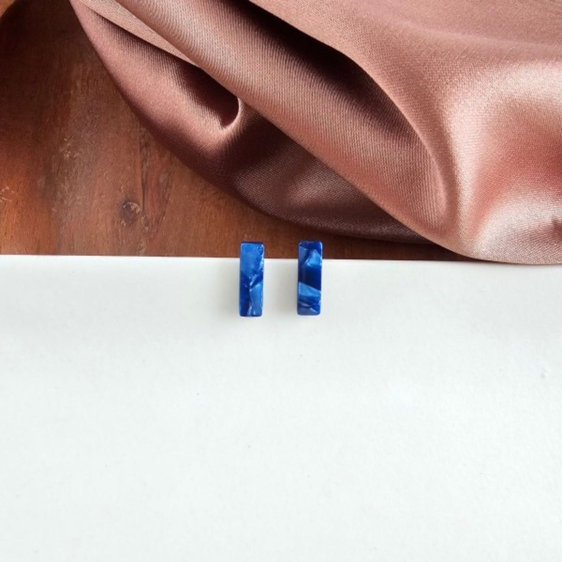 Blue rectangular earrings on a white surface with a brown fabric background