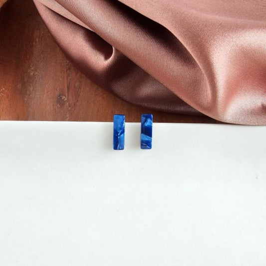 Blue rectangular earrings on a white surface with a brown fabric background