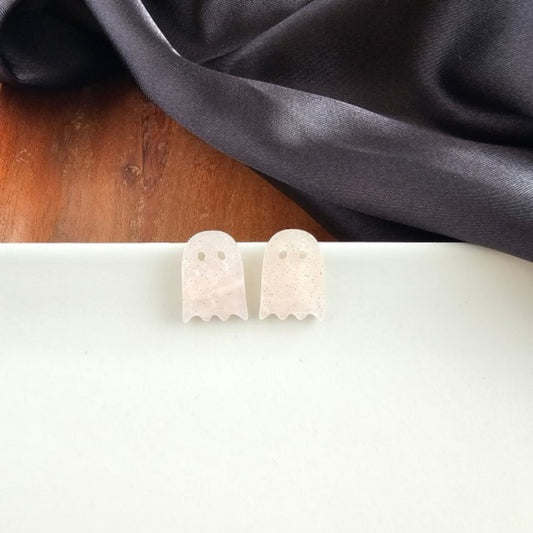 Ghost-shaped earrings on a white surface with a dark fabric background