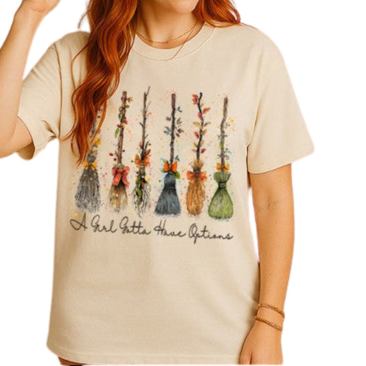 Beige t-shirt with colorful broom illustrations and text worn by a person.