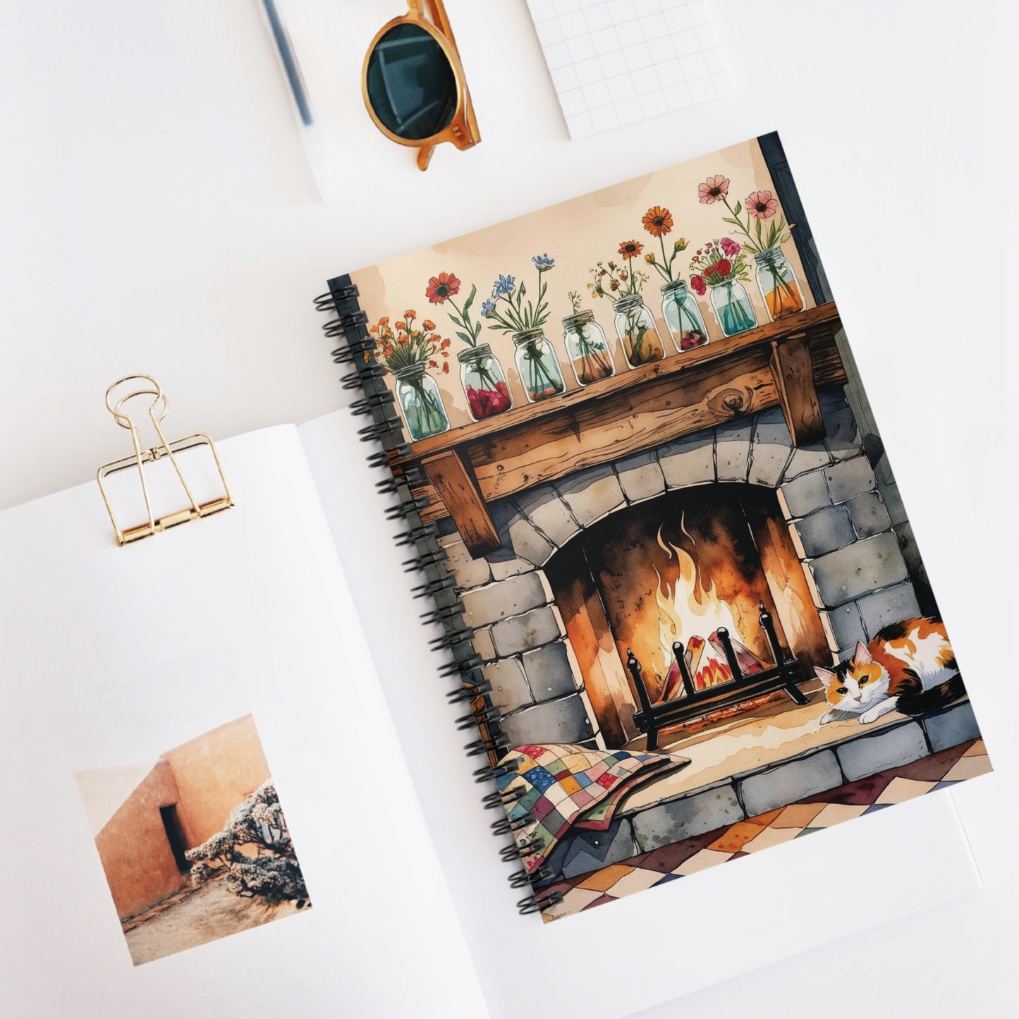 Notebook with a fireplace design on the cover, placed on a white surface with a photo and clip.