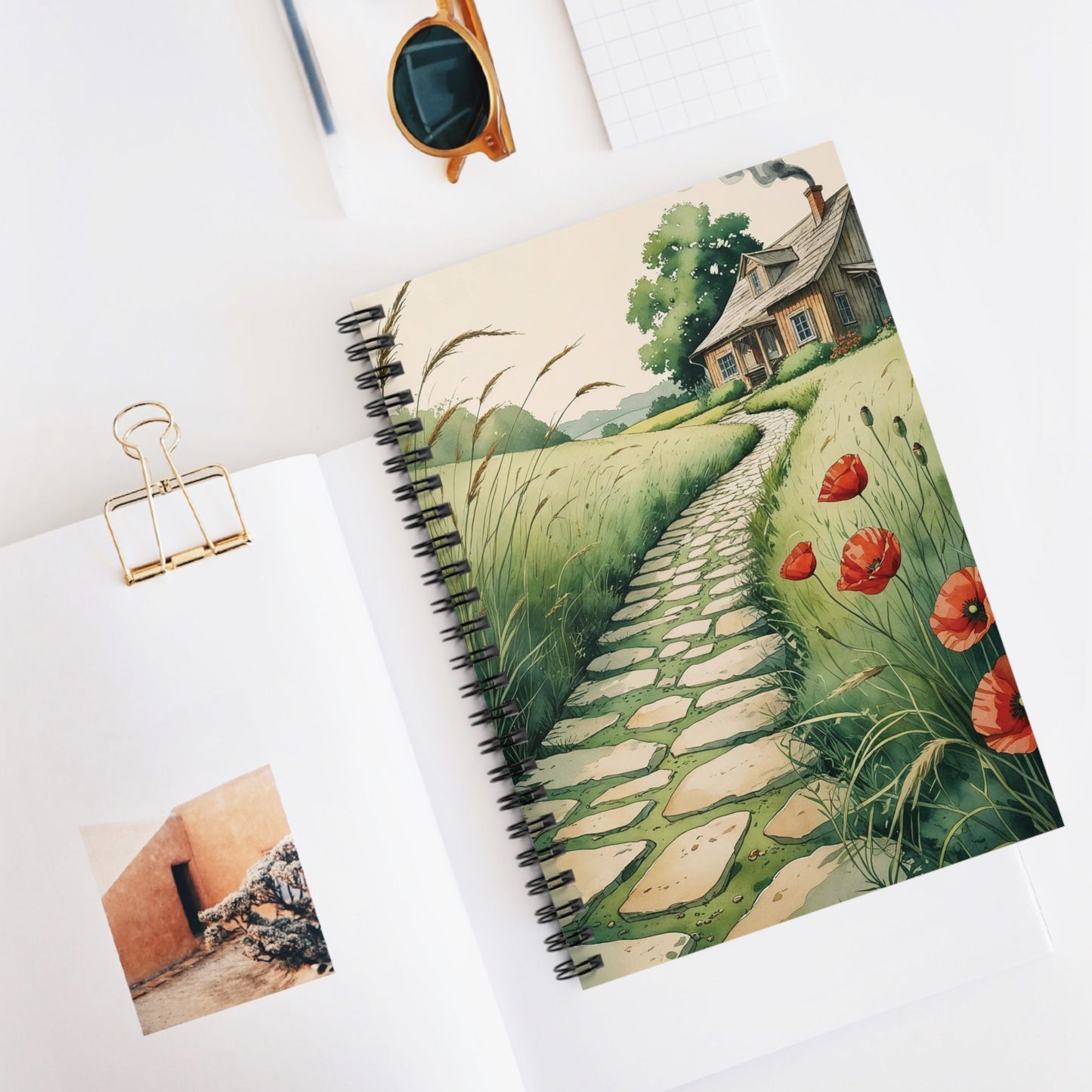 Notebook with a scenic cover featuring a house and path, on a white surface.