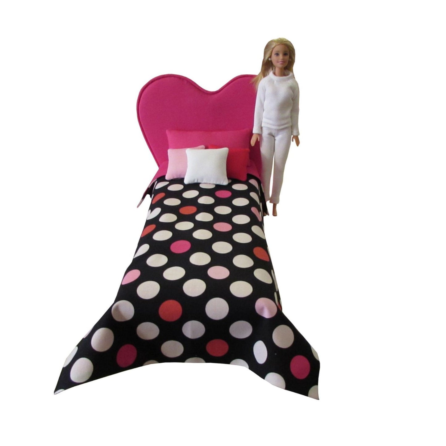 Barbie doll standing next to a bed with polka dot bedding and pink headboard on a white background