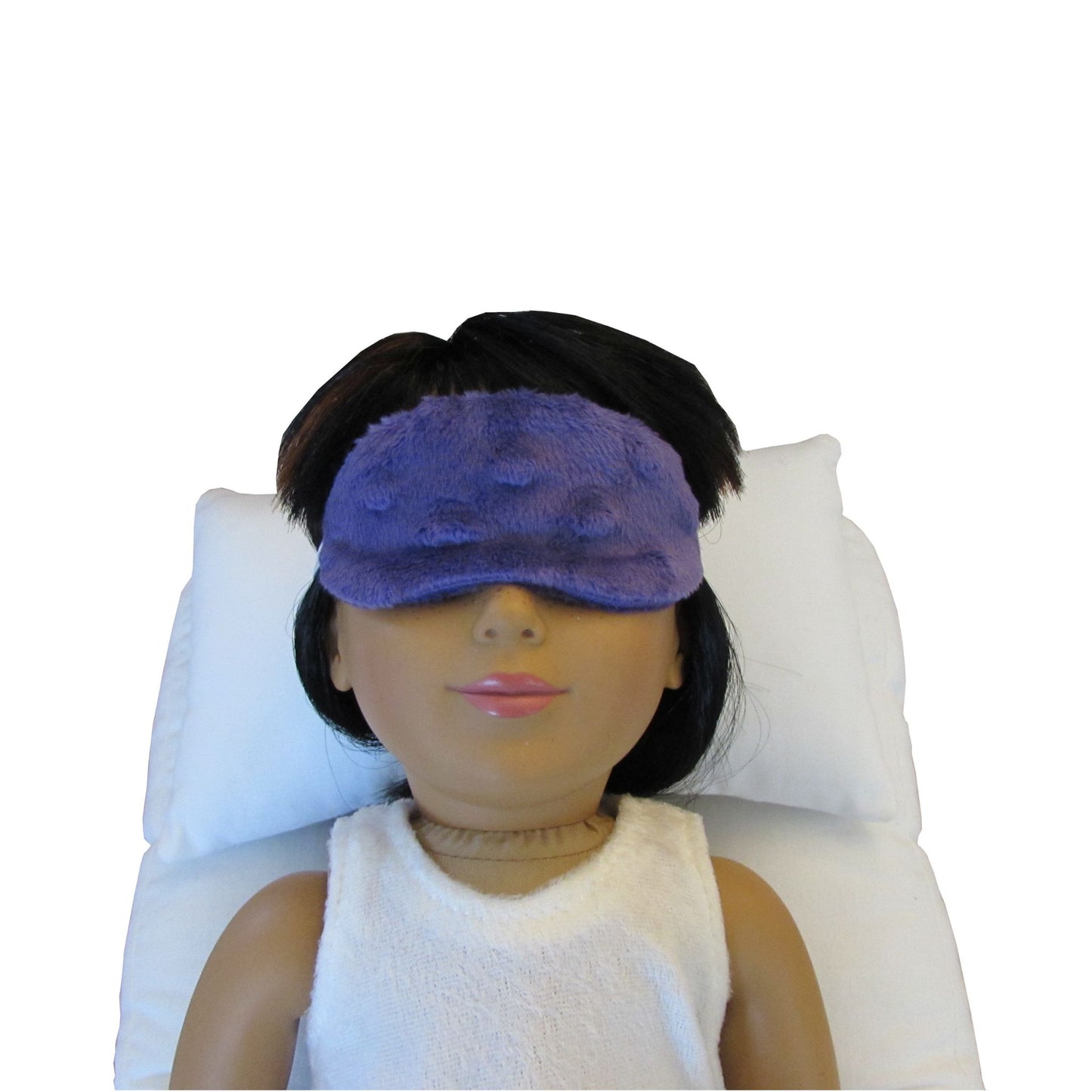 An 18-inch doll wearing a purple minky sleep mask while lying on a white doll pillow and a white doll mattress.