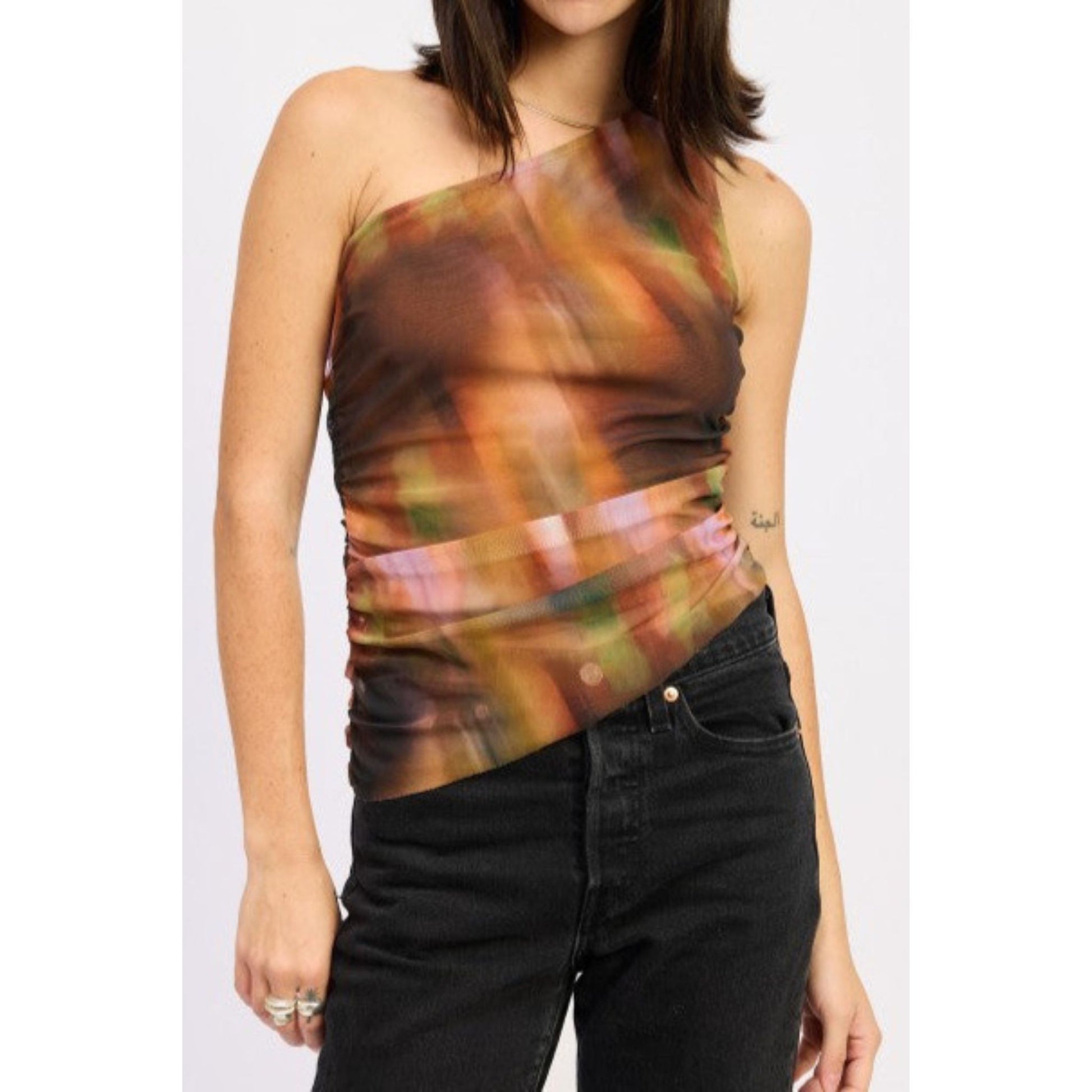 Woman wearing a colorful one-shoulder top and black pants on a white background