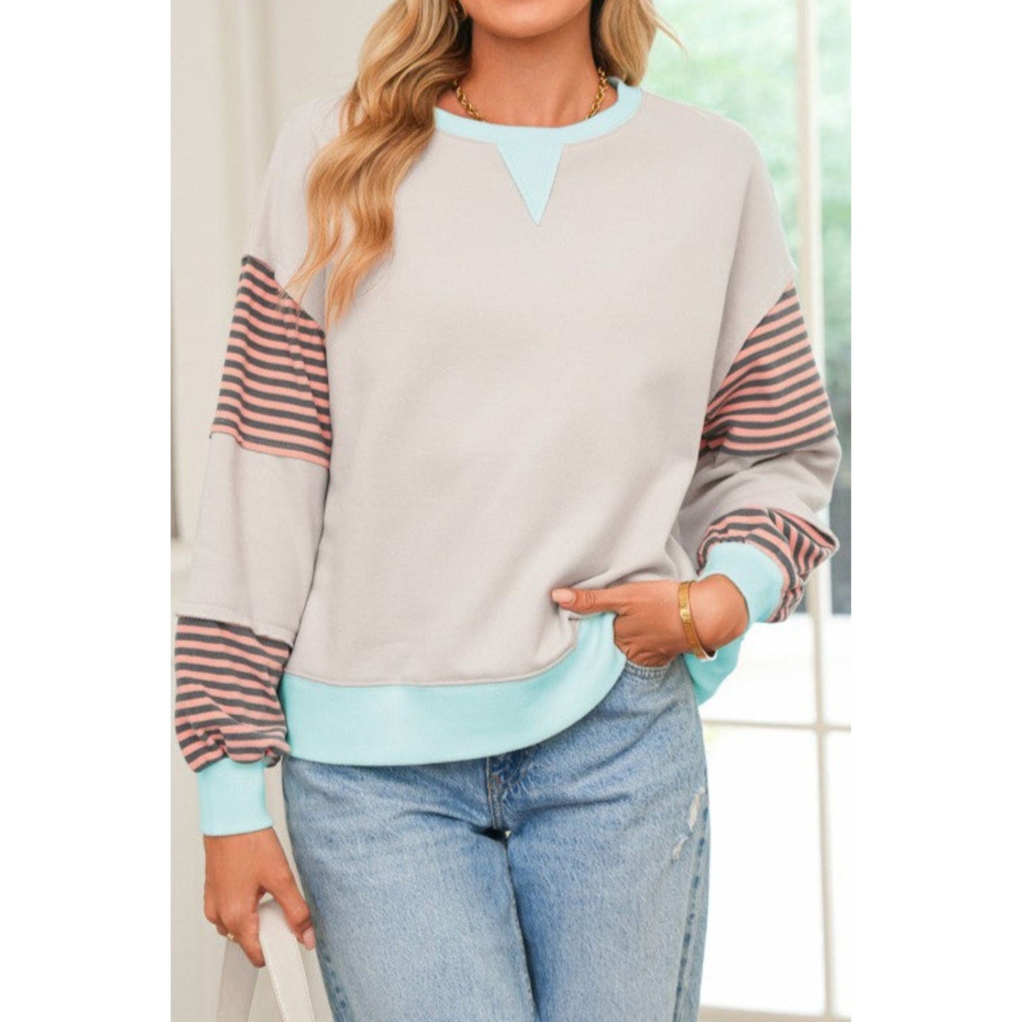 Woman wearing a gray sweater with colorful sleeves and light blue jeans indoors.