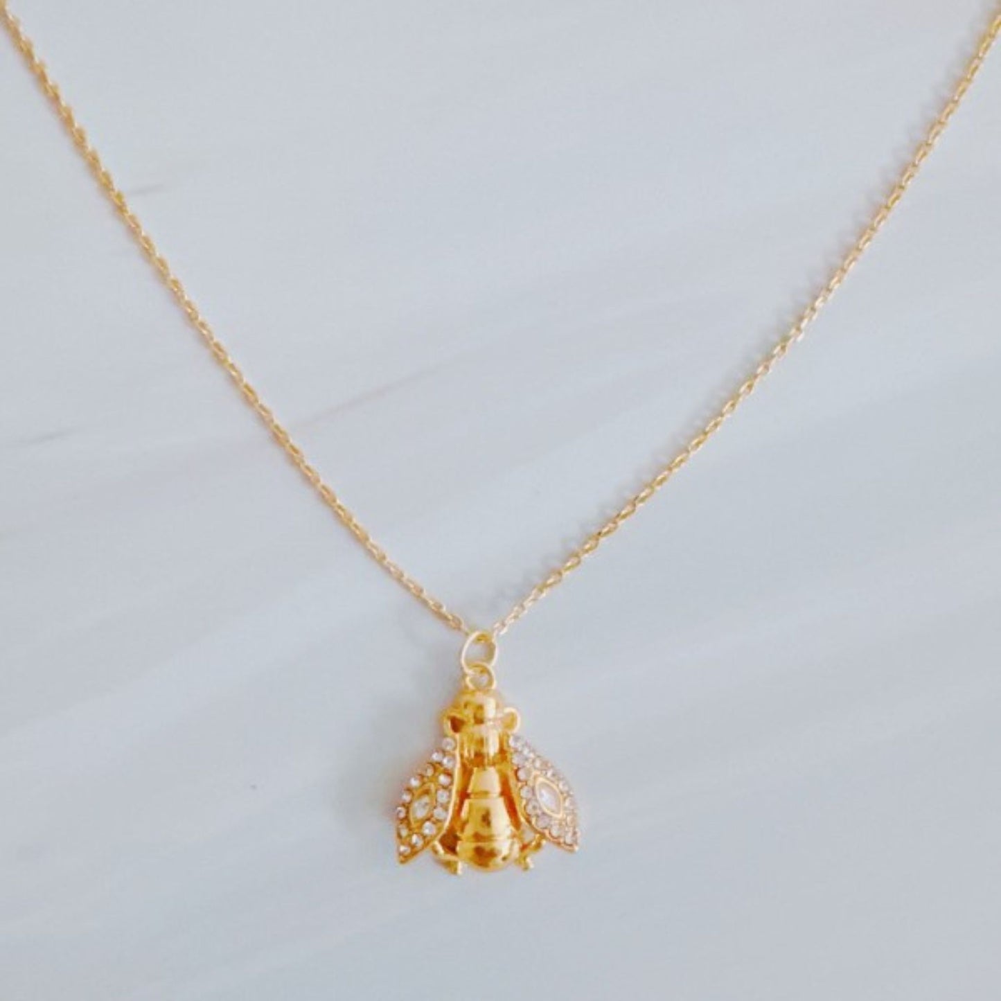 Gold bee-shaped pendant on a chain against a light gray background