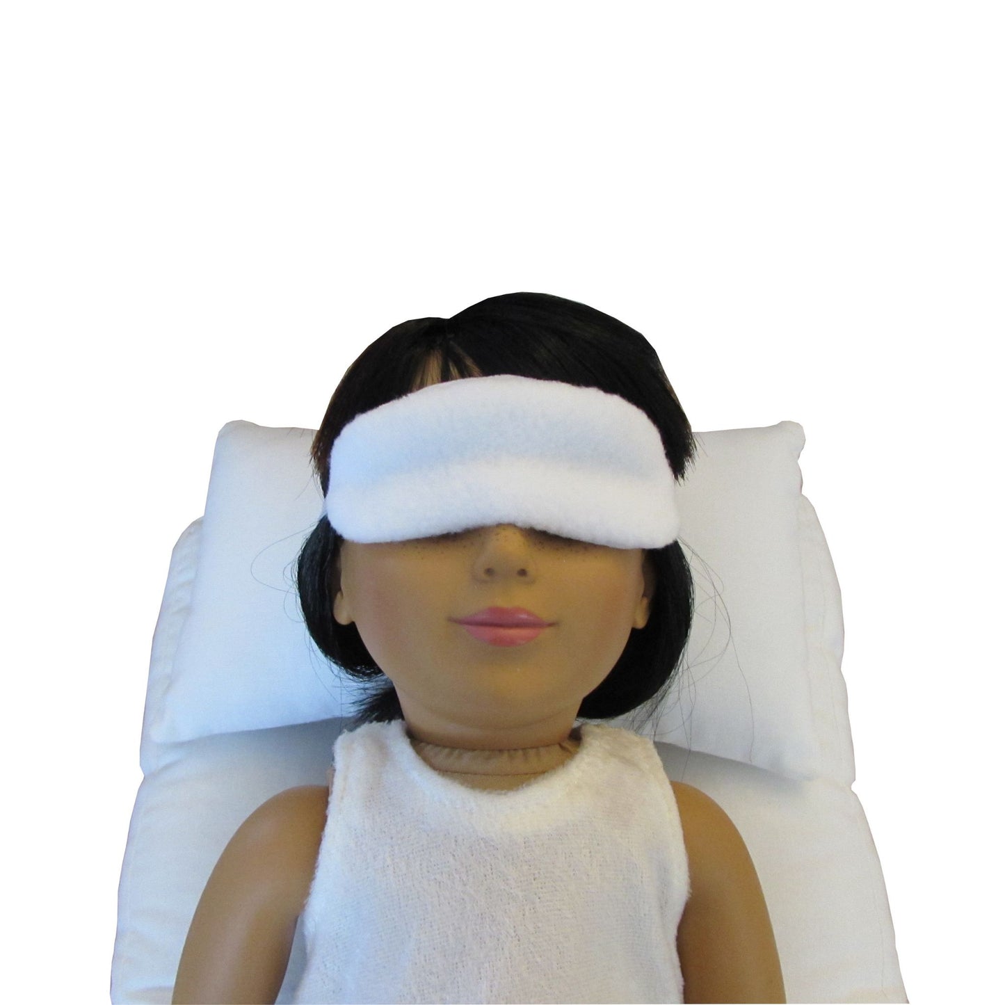 An 18-inch doll is wearing a white anti-pill fleece sleep mask while lying on a white doll pillow and a white doll mattress.