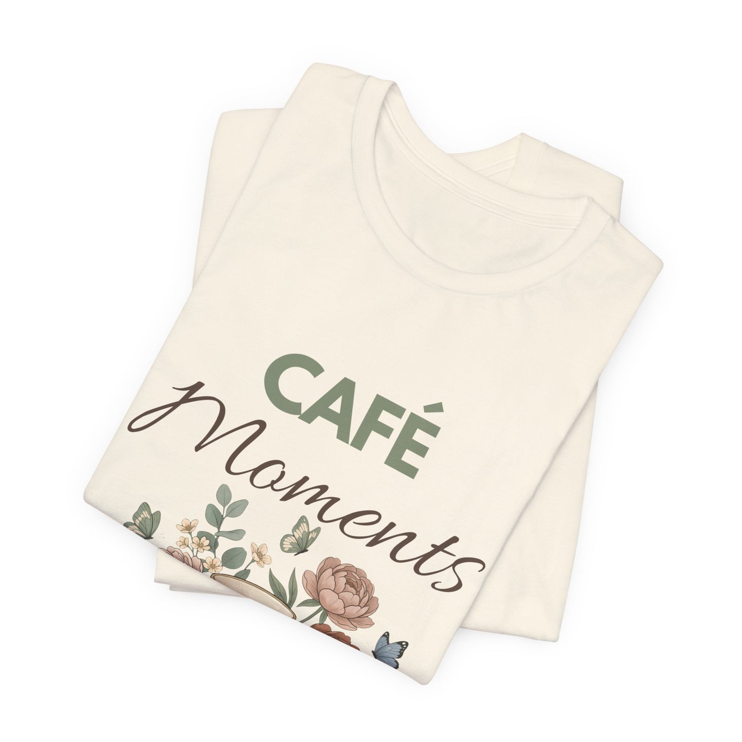 Folded natural colored t-shirt with 'Café Moments' text and floral design on a white background