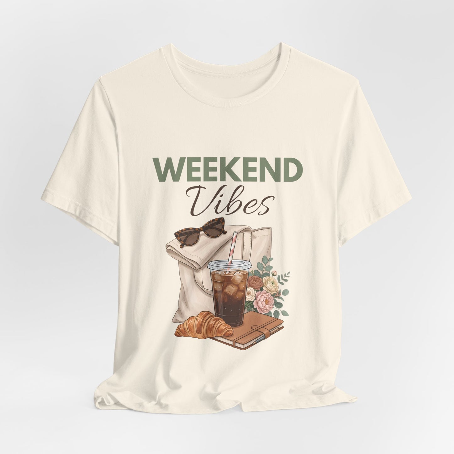 Natural colored t-shirt with 'Weekend Vibes' graphic design featuring a coffee cup, croissant, and sunglasses on a light gray background.
