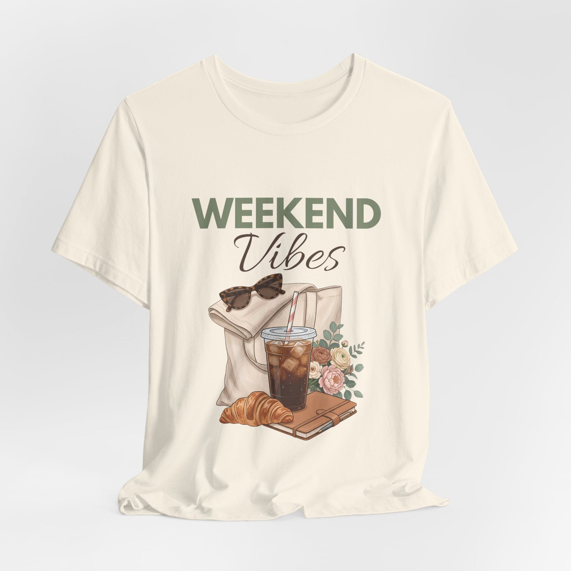 Natural colored t-shirt with 'Weekend Vibes' graphic design featuring a coffee cup, croissant, and sunglasses on a light gray background.