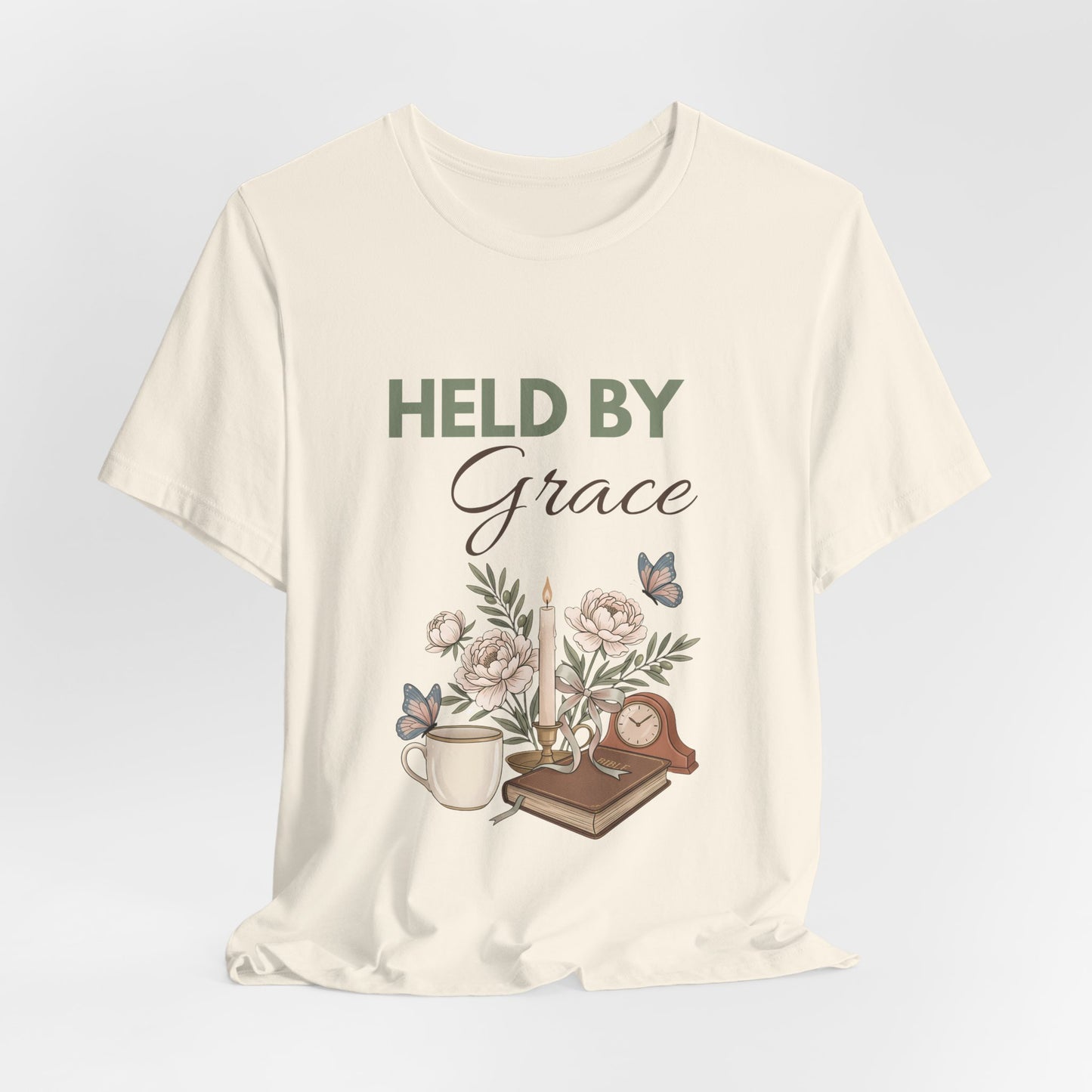 Natural colored t-shirt with 'HELD BY Grace' text and nature-themed design on a light gray background