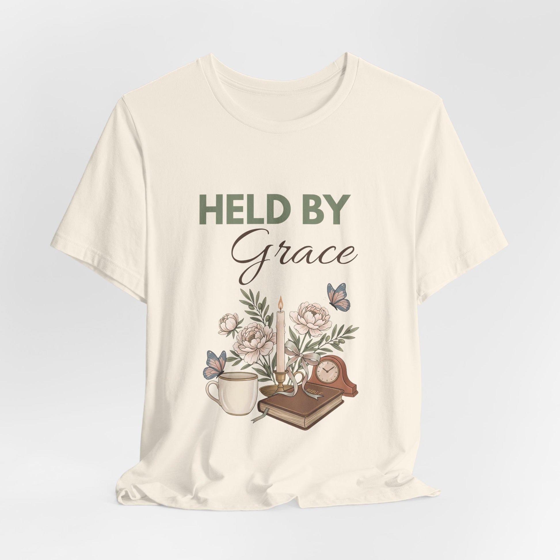 Natural colored t-shirt with 'HELD BY Grace' text and nature-themed design on a light gray background