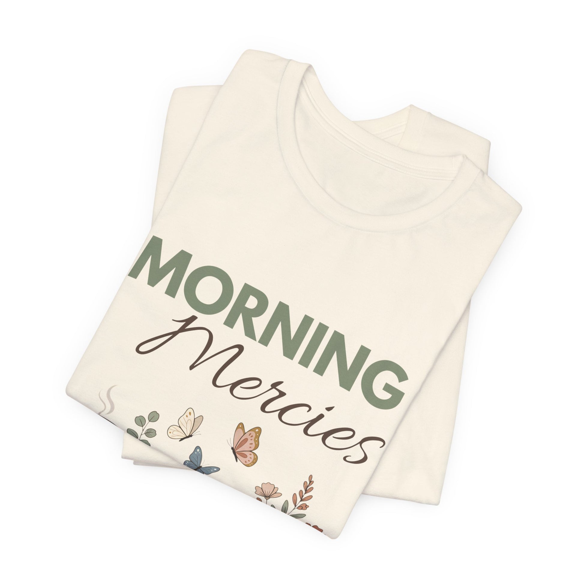 Folded natural colored t-shirt with 'Morning Mercies' text and butterfly design on a white background