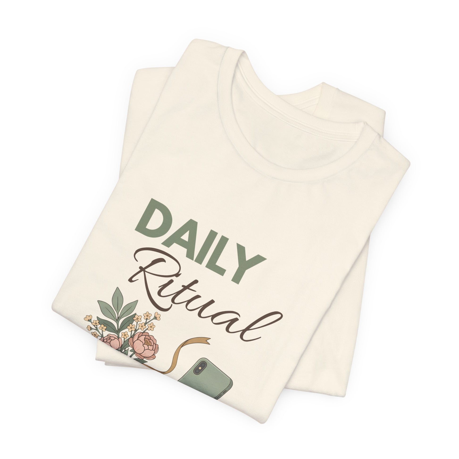 Folded natural colored t-shirt with 'Daily Ritual' text and floral design on a white background