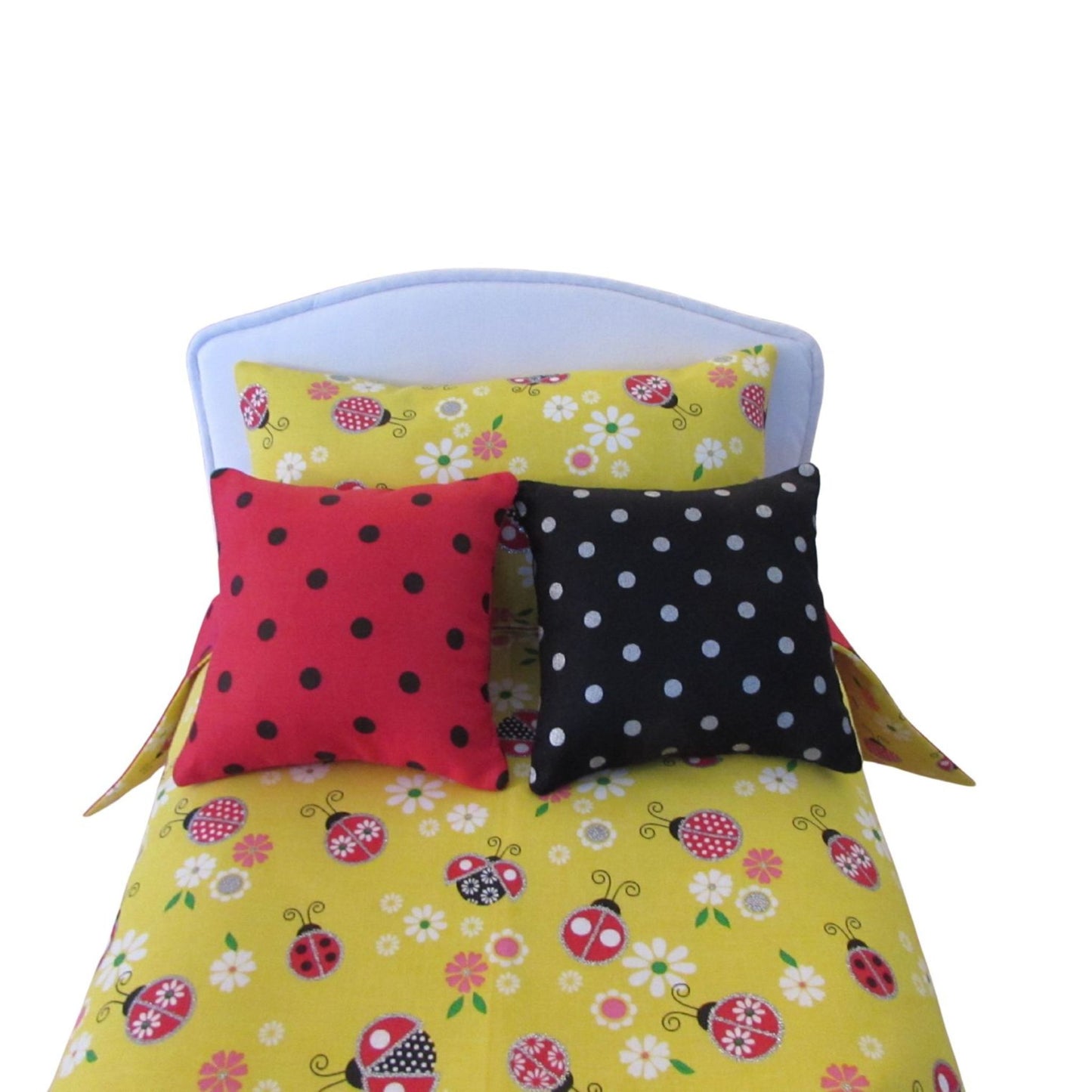 Doll bed with yellow floral and ladybug patterned bedding and two polka dot pillows.