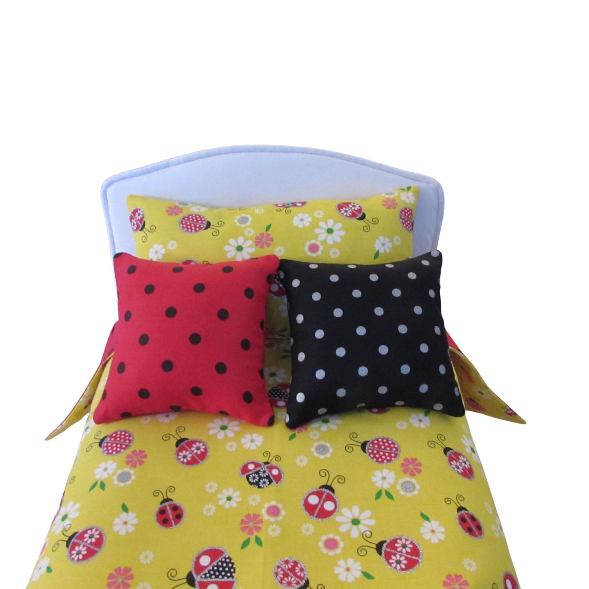 Doll bed with yellow floral and ladybug patterned bedding and two polka dot pillows.