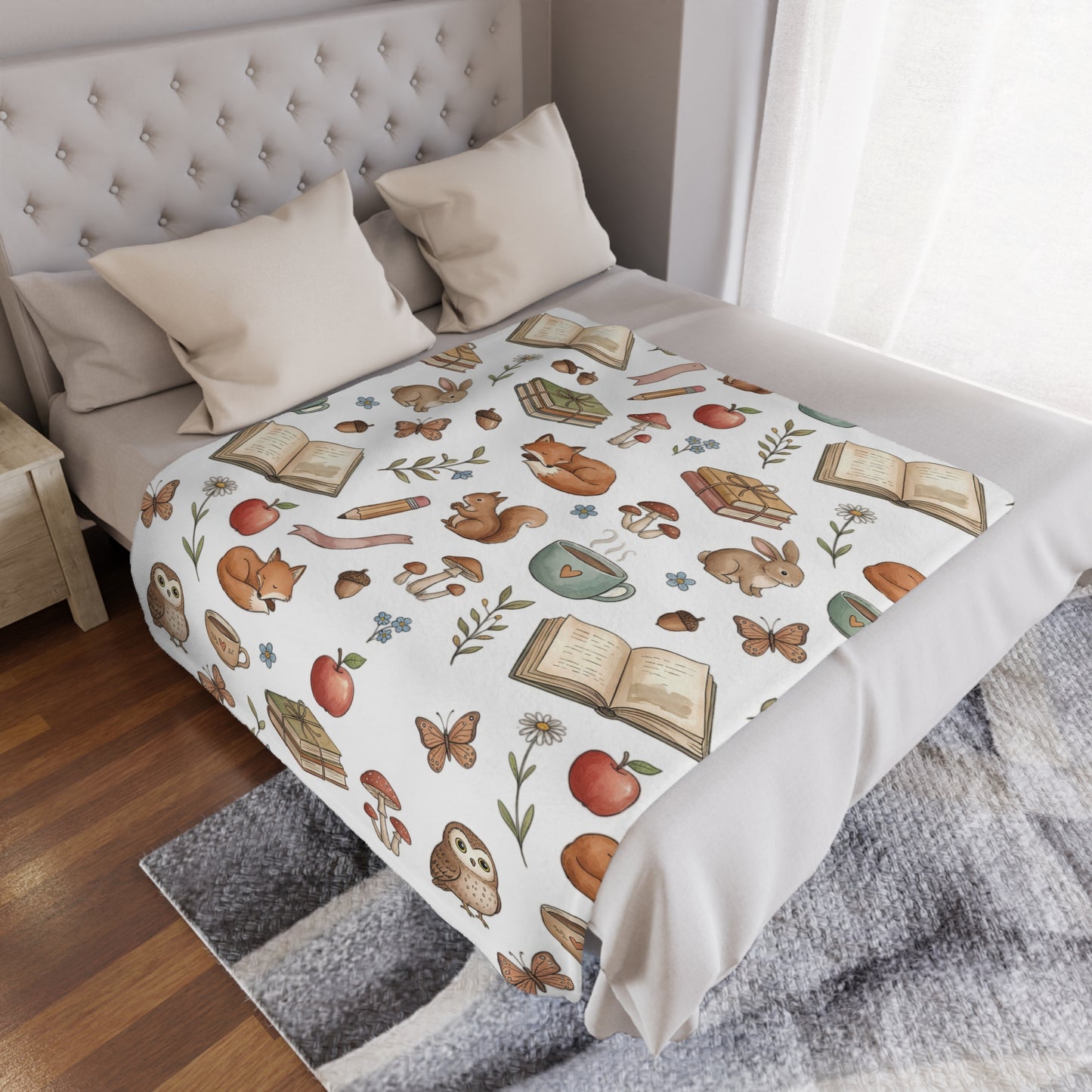 A white minky blanket featuring a whimsical woodland pattern of foxes, rabbits, owls, butterflies, open books, apples, and a teacup, styled on a bed in a bedroom setting.