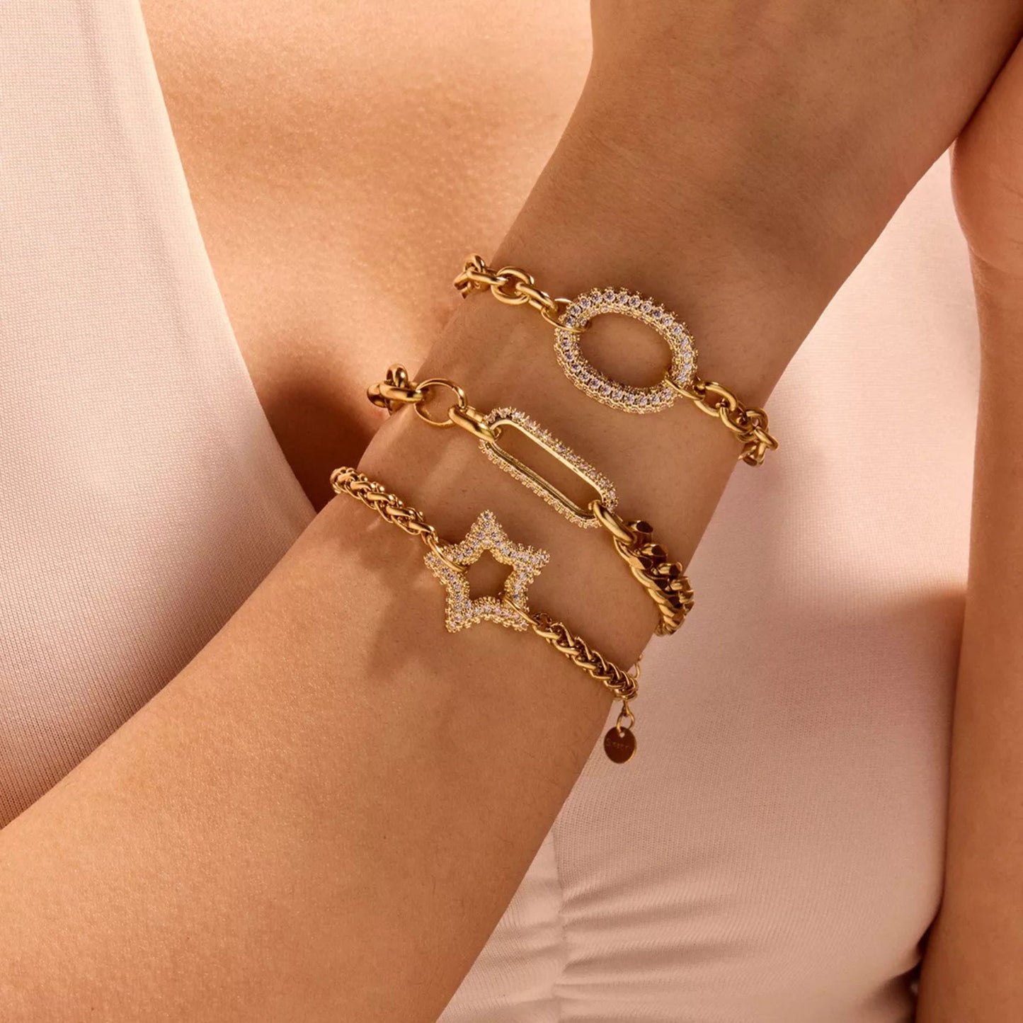 Gold bracelets with star and circular designs on a light pink background
