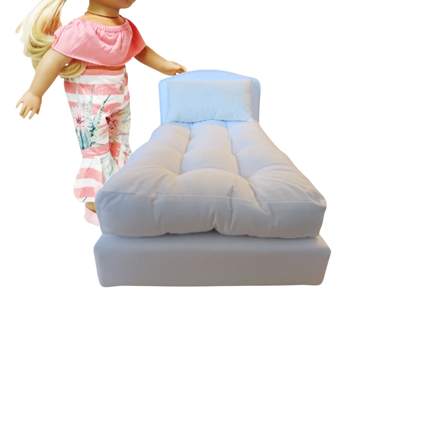 Dolll bed with white mattress next to a doll wearing a pink top and floral pants on a white background