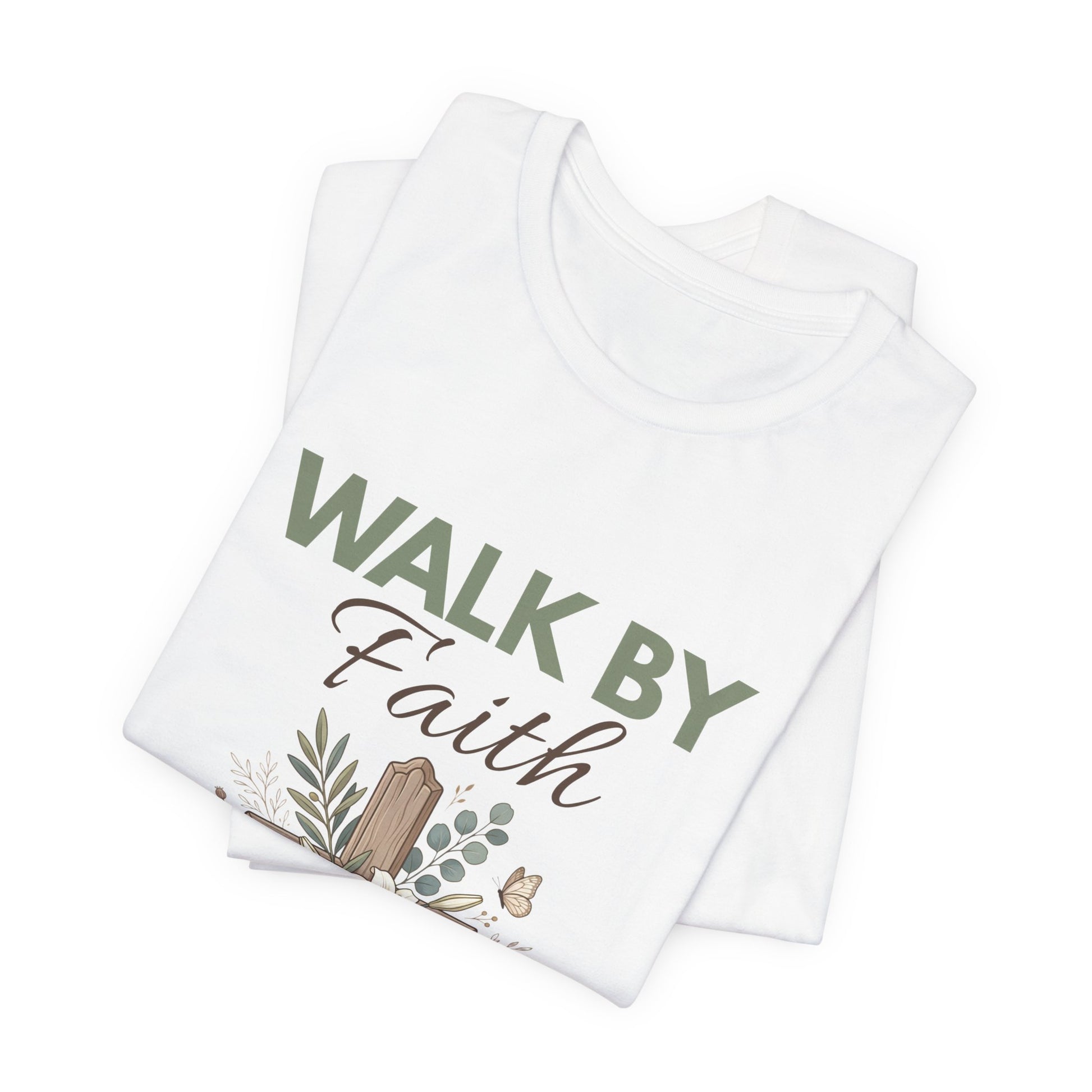 Folded white t-shirt with 'Walk by Faith' text and nature-themed design on a white background