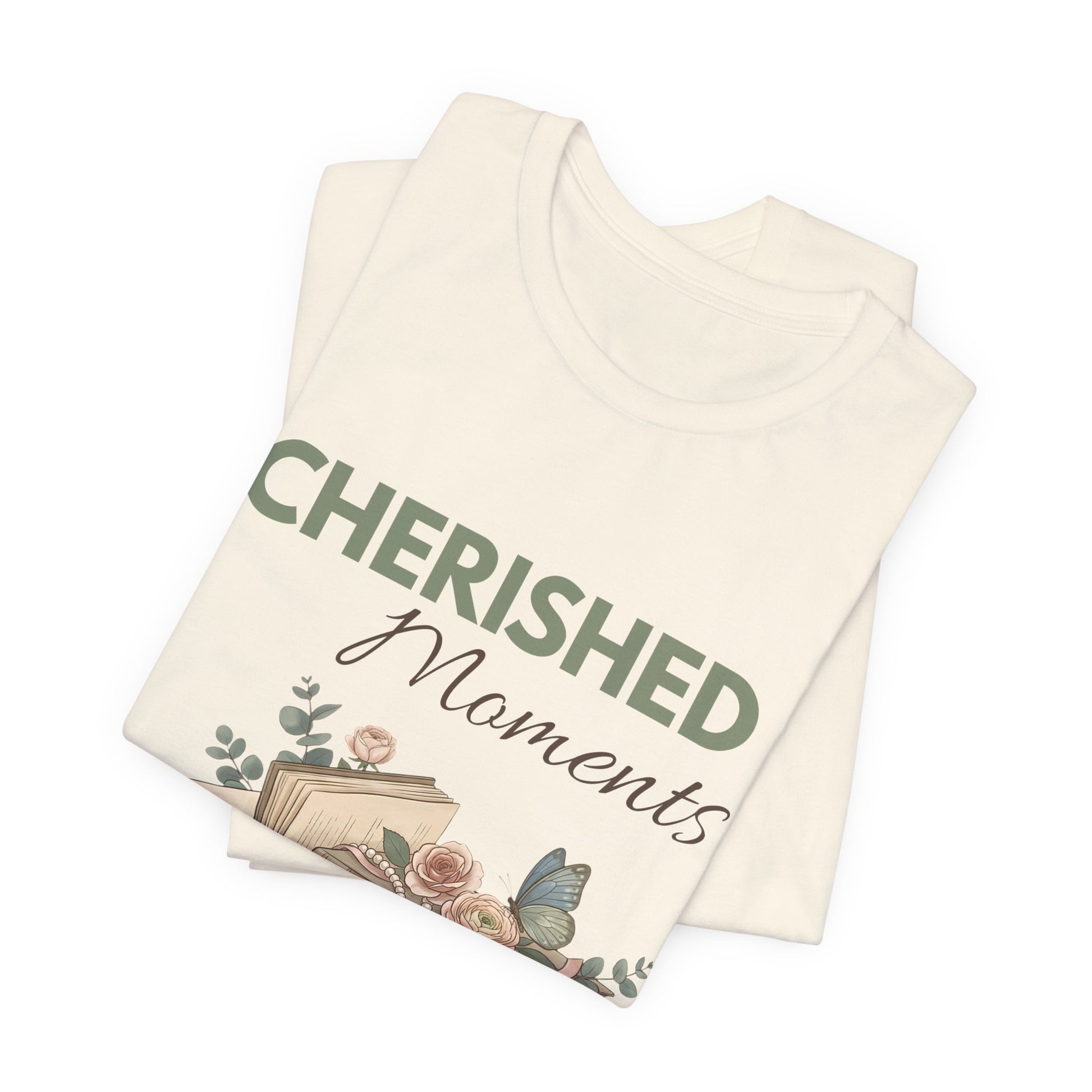A folded natural colored t-shirt with 'CHERISHED Moments' on the front.