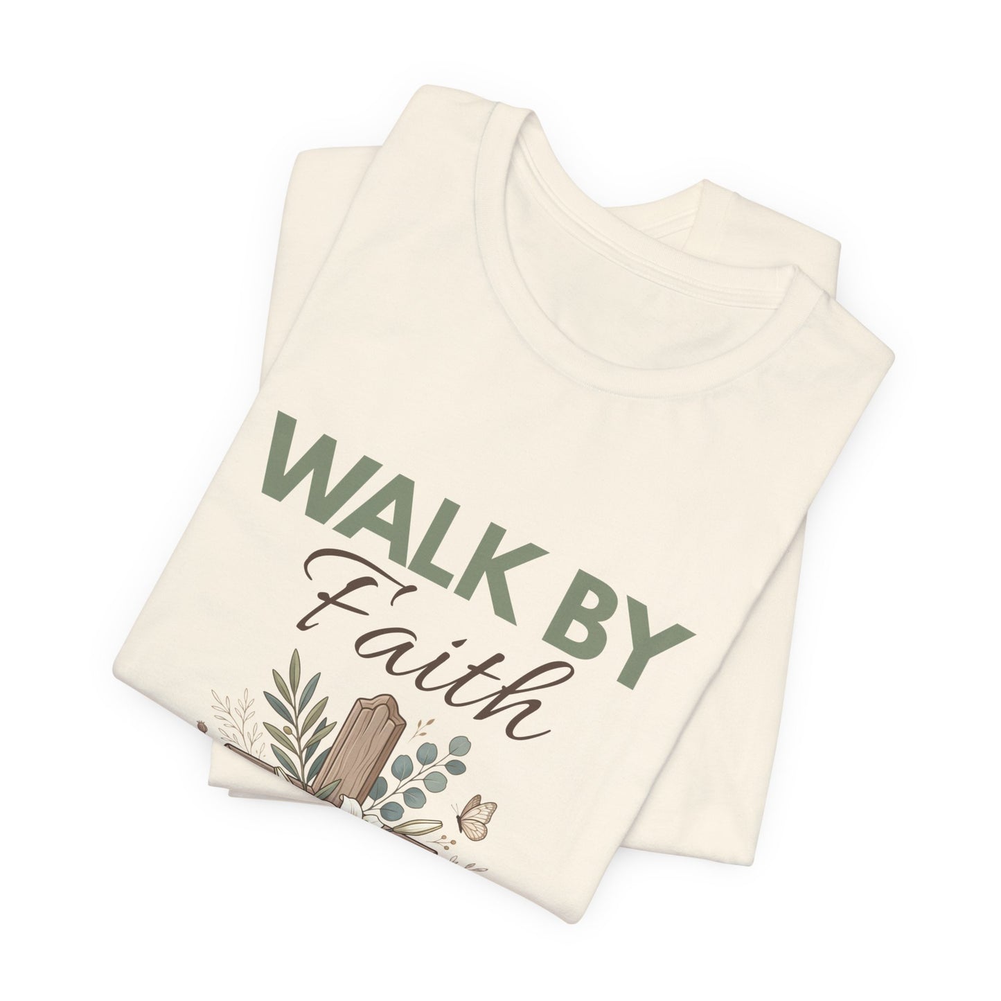 Folded natural colored t-shirt with 'Walk by Faith' text on a white background