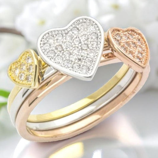 Three heart-shaped rings in gold, rose gold, and silver on a blurred background