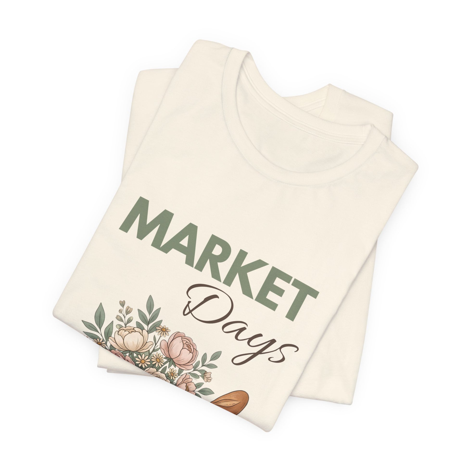 A folded natural colored t-shirt with 'Market Days' on the front.
