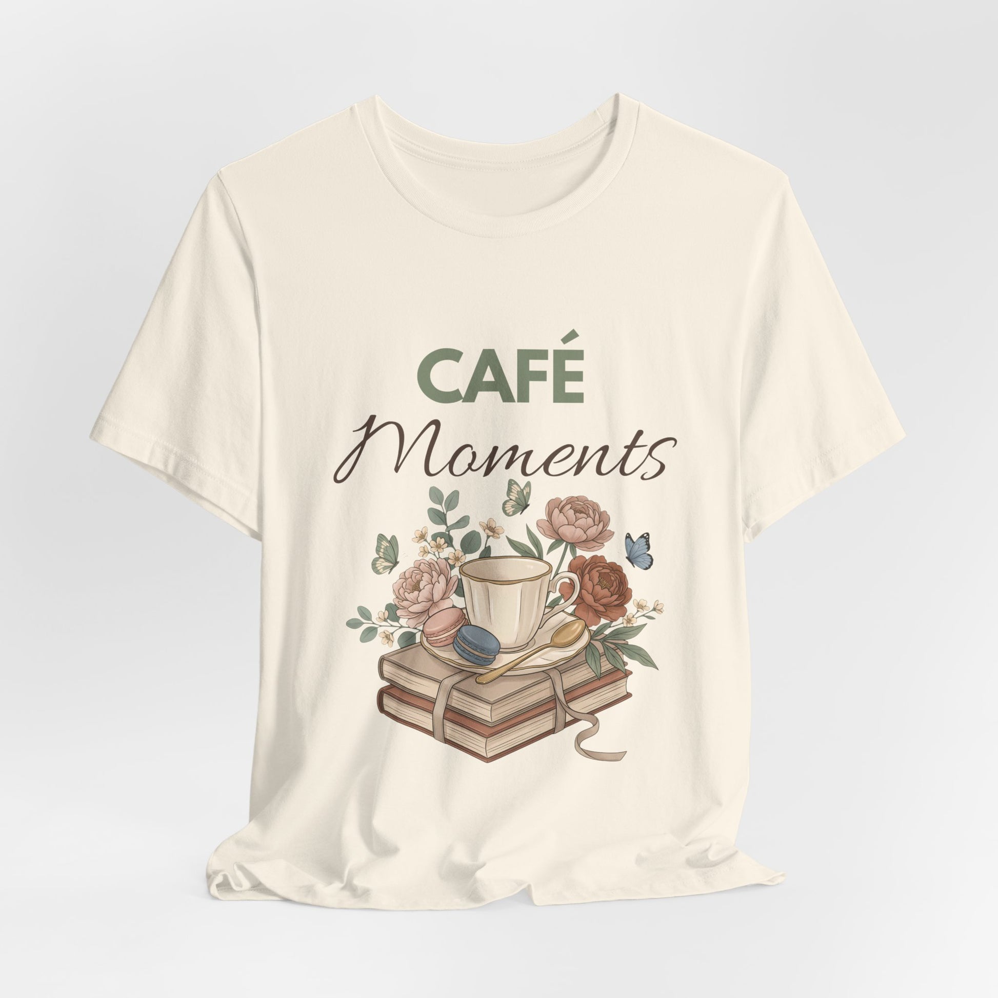 Natural colored t-shirt with 'Café Moments' design featuring a cup, books, and flowers on a light gray background