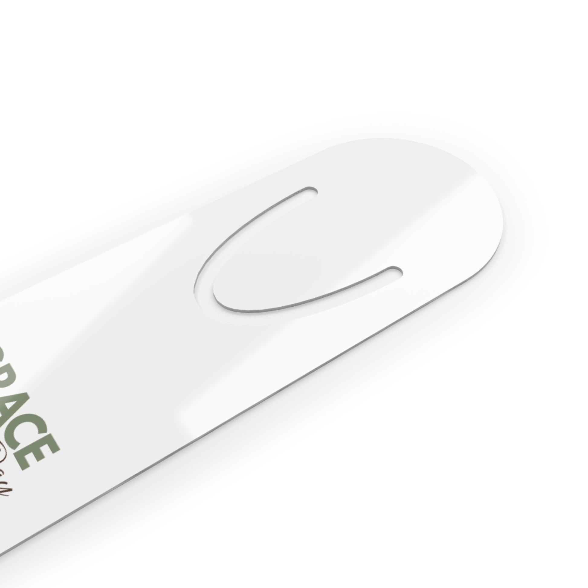 A close-up of a glossy white metal bookmark with a cutout and partial green text reading 'GRACE' on a white background.