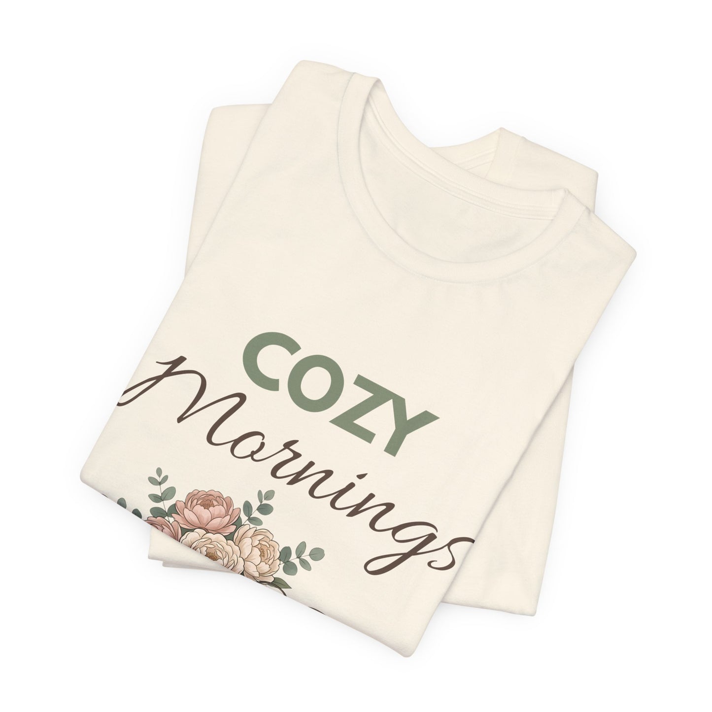 Folded natural colored t-shirt with 'Cozy Mornings' text and floral design on a white background