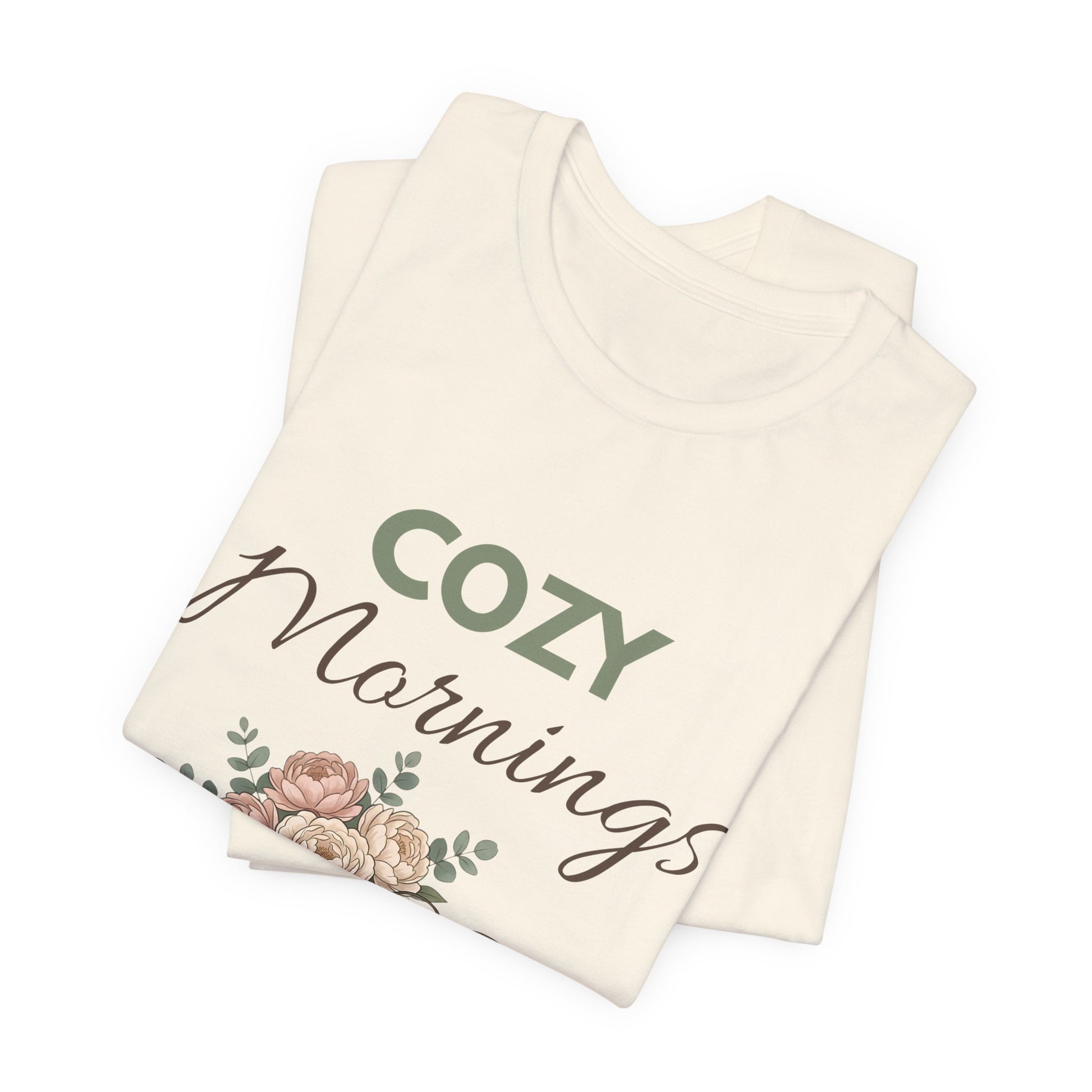 Folded natural colored t-shirt with 'Cozy Mornings' text and floral design on a white background