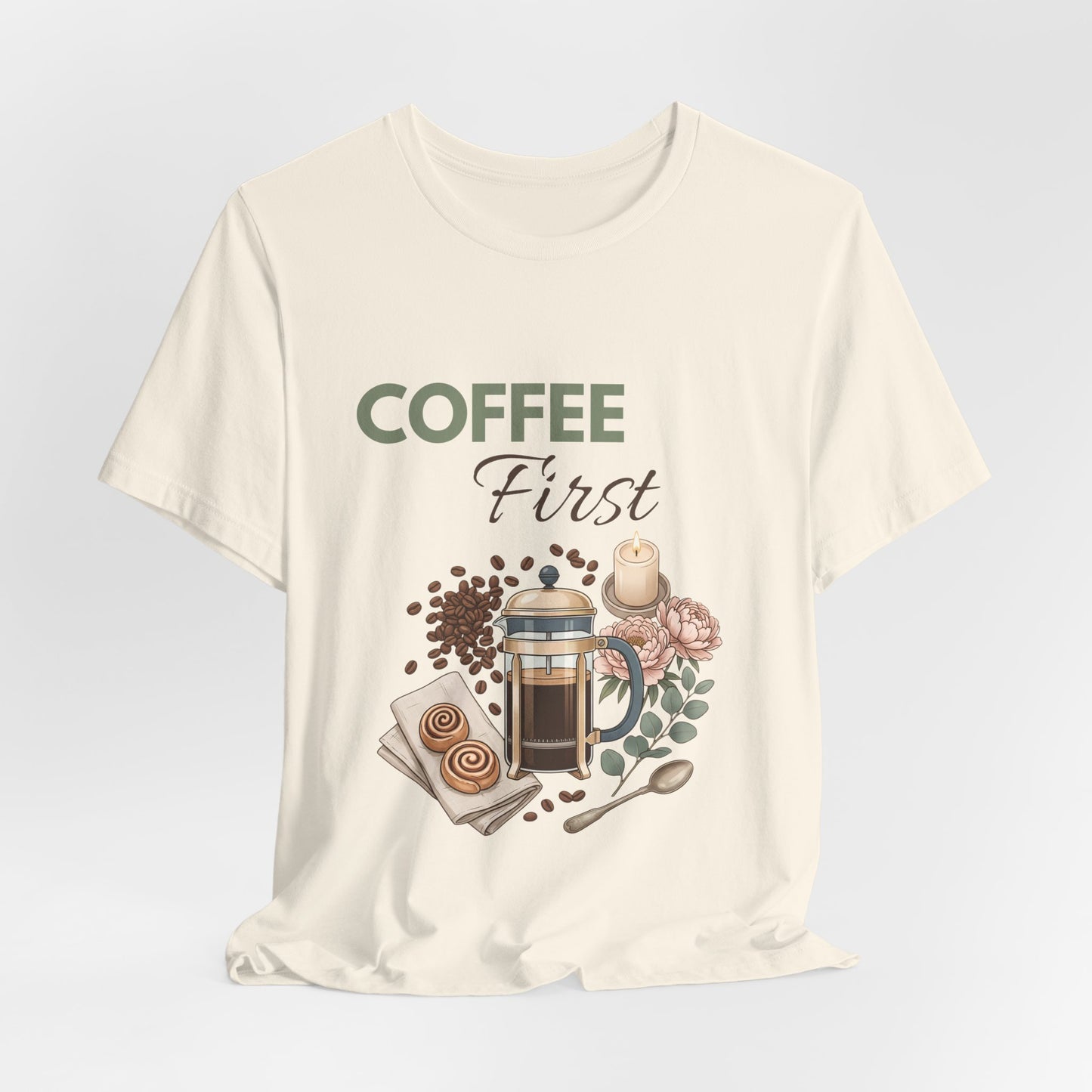 Natural colored t-shirt with 'Coffee First' text and coffee-themed graphics on a light gray background