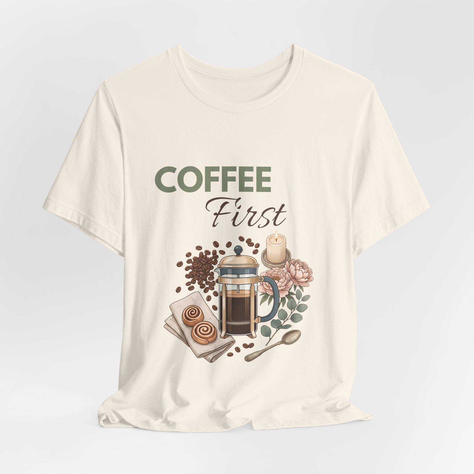 Natural colored t-shirt with 'Coffee First' text and coffee-themed graphics on a light gray background